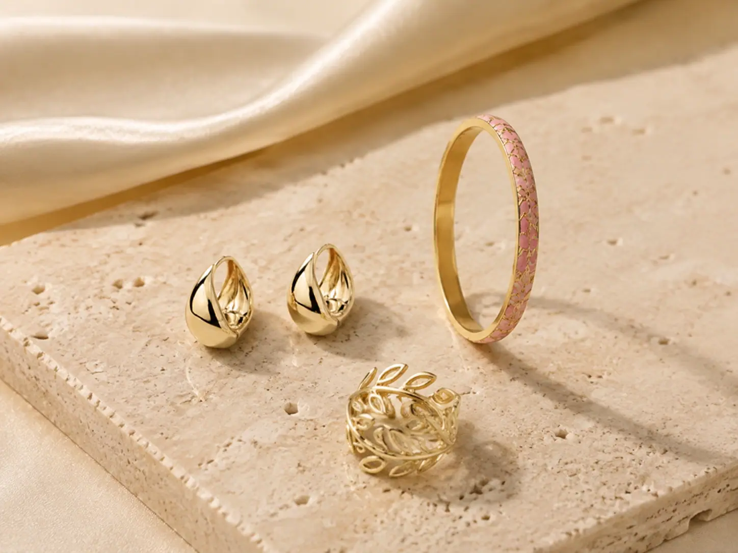 Sélection de bijoux dorés RAJ sur travertin et soie ivoire